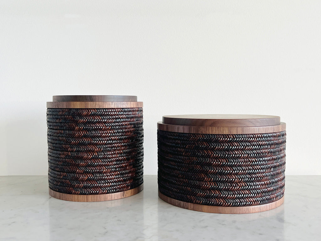 Two cylindrical woven baskets on a marble surface with a white background