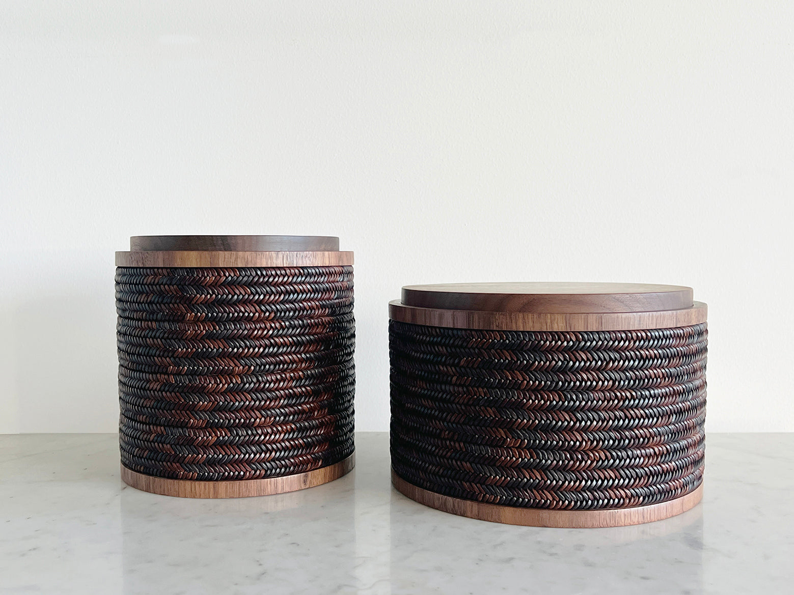 Two cylindrical woven baskets on a marble surface with a white background